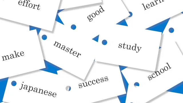 「努力」「未来」「学ぶ」「英語」「作る」「マスターする」など、単語が黒文字で印刷された白いフラッシュカードが散在して配置されています。背景は青で、白い三角形があります。