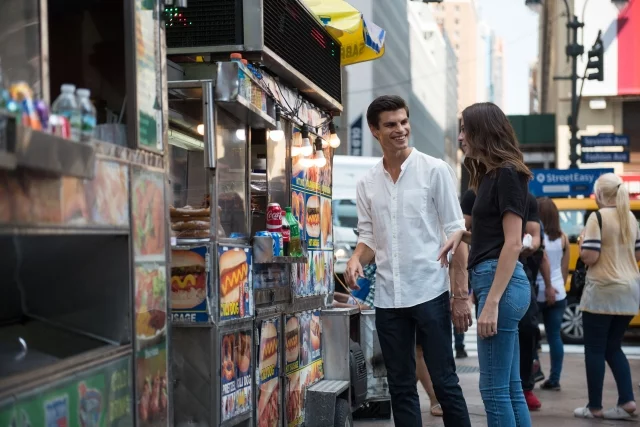 ニューヨークのストリートフードスタンドでホットドッグを注文するカップルの写真。都会の雰囲気。